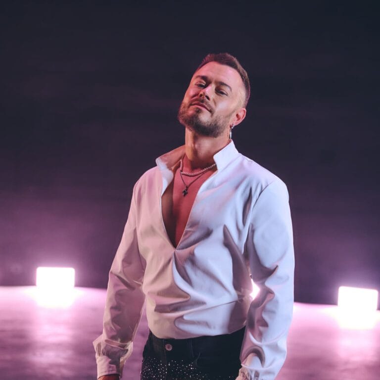 Simon Rosc v beli srajci med promocijskim fotografiranjem na odru z osvetlitvijo.